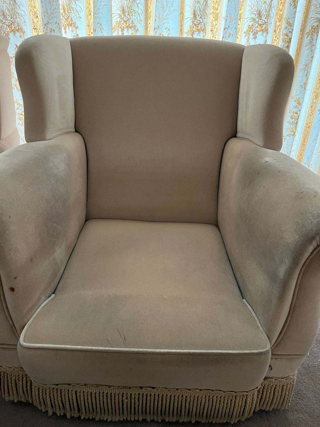 A cream wingback armchair before cleaning, with soiling down both arms and around the seat cushion