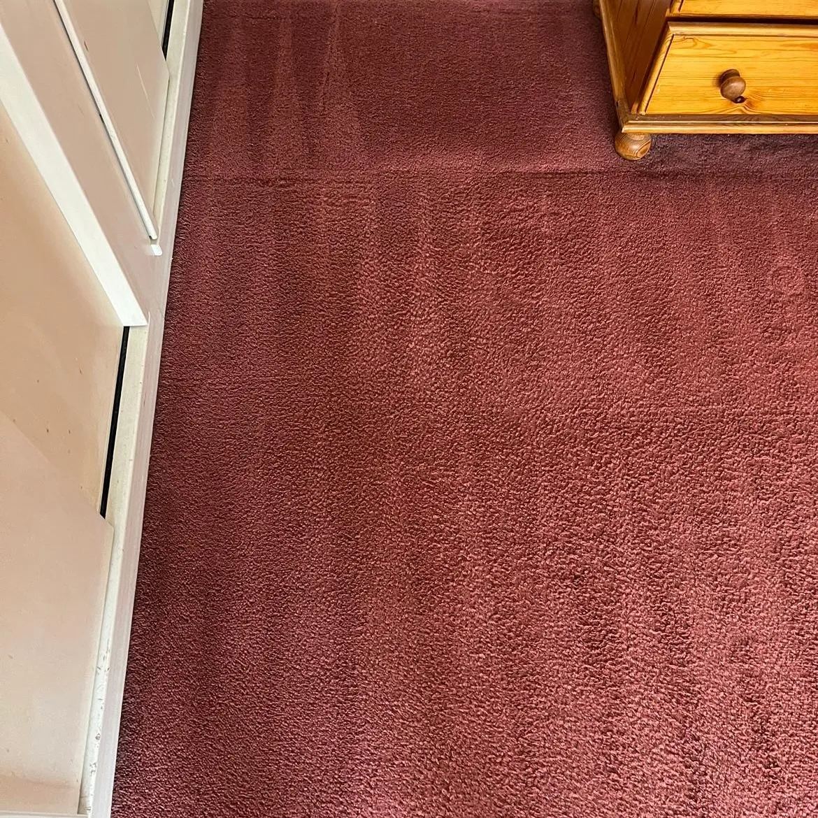 The same red bedroom carpet after cleaning, the marks gone and the colour even across the floor
