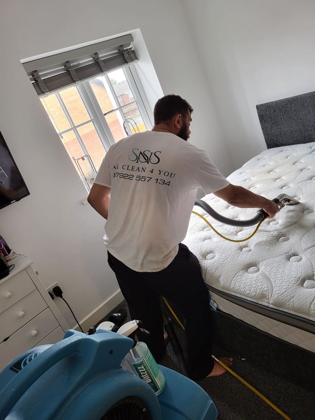 Shane cleaning a double mattress in place with a handheld tool, the air mover running beside the bed