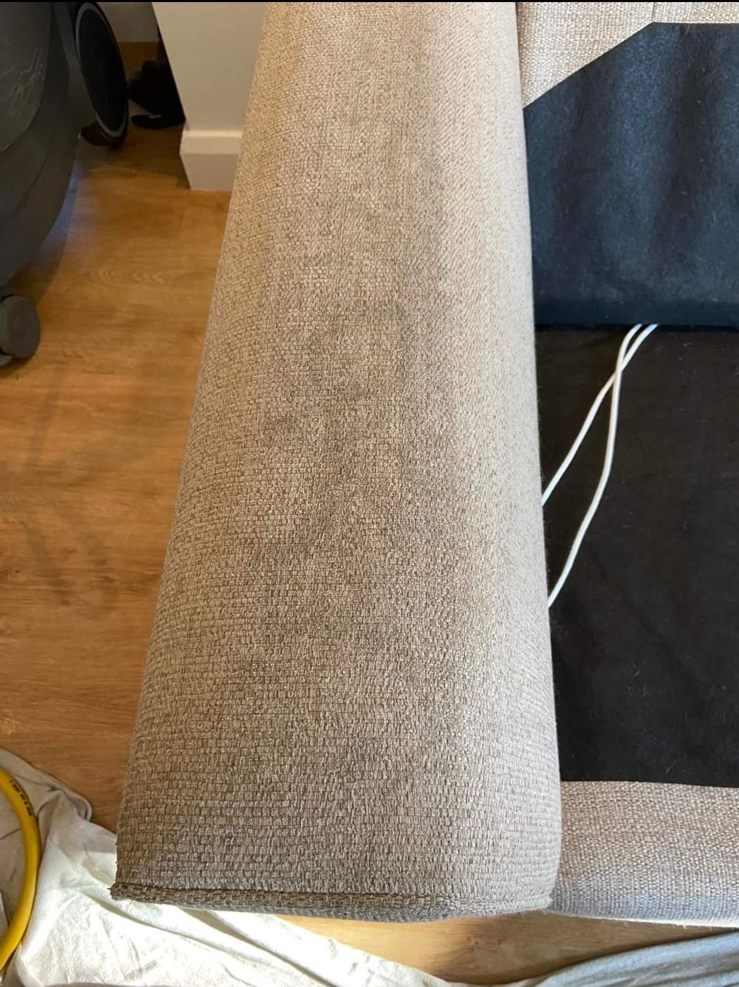 The arm of a beige fabric sofa before cleaning, darkened where hands and heads have rested against it